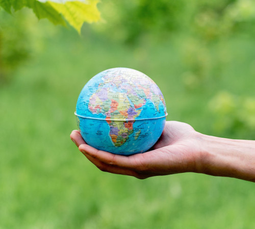 Mano sujetando la bola del mundo y de fondo un paisaje verde
