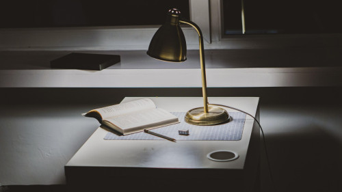 Un escritorio en la oscuridad, donde un flexo ilumina un libro abierto. Imagen de Yury Rymko en Pixabay